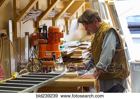 Stock Photo - Caucasian carpenter writing on notepad in workshop. Fotosearch