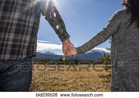 Stock Photo - Caucasian couple holding hands in field. Fotosearch