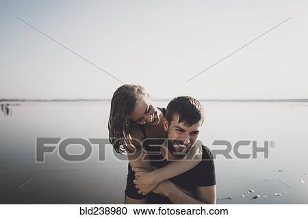 Stock Image - Caucasian couple hugging near lake. Fotosearch