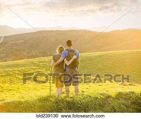 Stock Image - Caucasian couple hugging on hill. Fotosearch