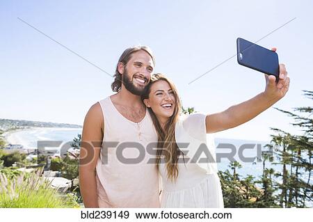 Stock Photo - Caucasian couple posing for cell phone selfie at beach. Fotosearch