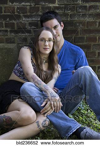Stock Image - Caucasian couple sitting on ground leaning on wall. Fotosearch