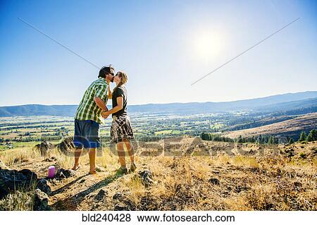 Stock Photo - Caucasian couple standing on hill and kissing. Fotosearch