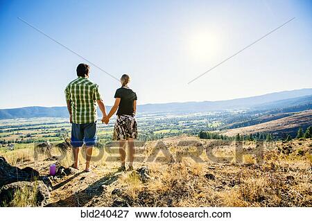 Stock Photo - Caucasian couple standing on hill holding hands. Fotosearch