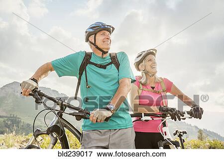 Stock Photo - Caucasian couple standing with mountain bikes. Fotosearch