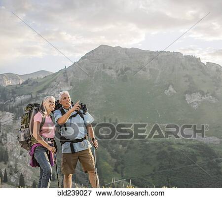 Stock Photo - Caucasian couple with binoculars hiking on mountain. Fotosearch