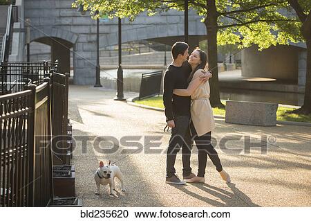 Stock Image - Caucasian couple with dog hugging in park. Fotosearch