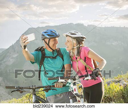 Caucasian couple with mountain bikes posing for cell phone selfie View Large Photo Image Picture - Caucasian couple with mountain bikes posing for cell phone selfie. Fotosearch