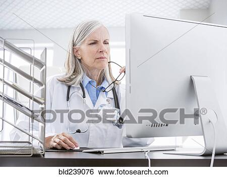 Stock Photograph - Caucasian doctor using computer at desk. Fotosearch