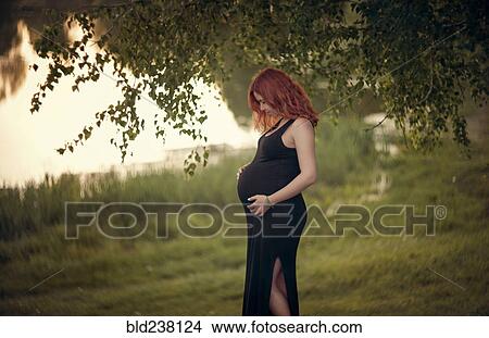 Caucasian expectant mother holding belly under tree branches View Large Photo Image Picture - Caucasian expectant mother holding belly under tree branches. Fotosearch