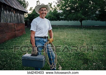 Stock Image - Caucasian farmer carrying rope and toolbox. Fotosearch