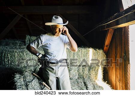Stock Image - Caucasian farmer in barn talking on cell phone. Fotosearch