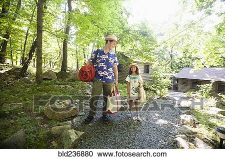 Stock Image - Caucasian father and daughter carrying bags at cabin. Fotosearch