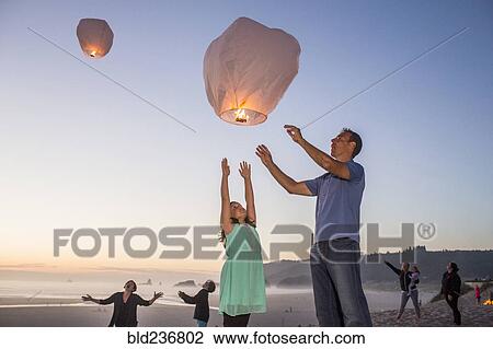 Stock Image - Caucasian father and daughter flying lantern balloon at beach. Fotosearch