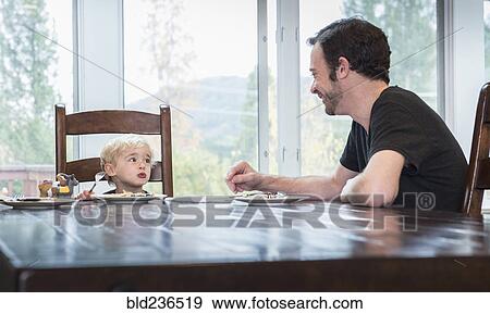 Stock Photo - Caucasian father and son eating food at table. Fotosearch