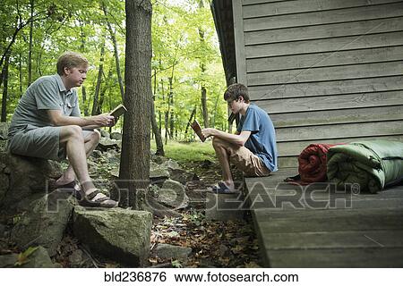 Stock Photograph - Caucasian father and son reading books at cabin. Fotosearch