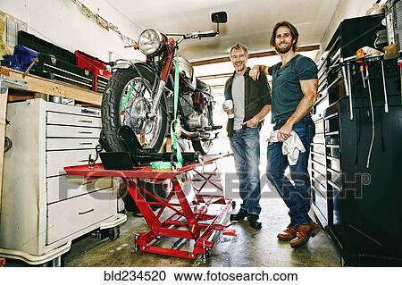 Stock Image - Caucasian father and son repairing motorcycle in garage. Fotosearch