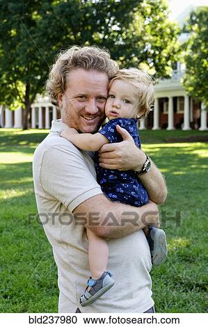 Stock Image - Caucasian father holding baby son outdoors. Fotosearch