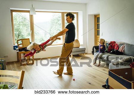 Stock Photograph - Caucasian father spinning daughter by arm and leg in livingroom. Fotosearch