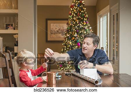 Stock Photograph - Caucasian fathers and son wrapping Christmas gift. Fotosearch