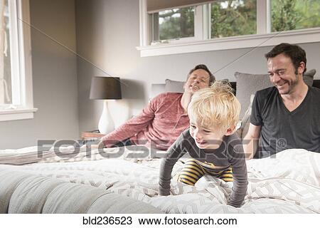 Stock Image - Caucasian fathers playing on bed with son. Fotosearch