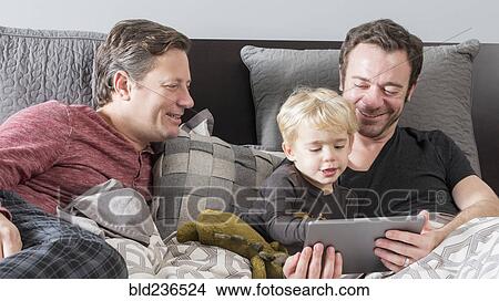 Caucasian fathers using digital tablet on bed with son View Large Photo Image Picture - Caucasian fathers using digital tablet on bed with son. Fotosearch