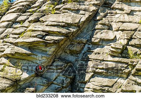 Stock Photo - Caucasian friends climbing mountain with rope. Fotosearch