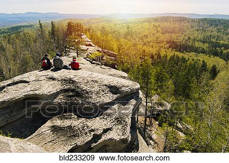 Caucasian friends sitting on mountain rock admiring scenic view View Large Photo Image Stock Photo - Caucasian friends sitting on mountain rock admiring scenic view. Fotosearch