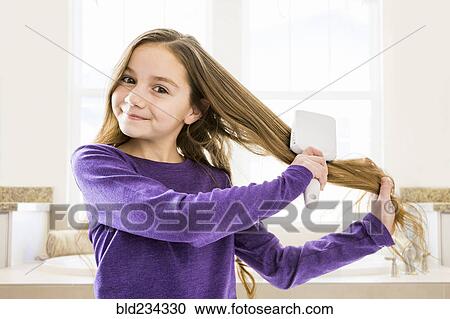 Stock Image - Caucasian girl brushing hair in bathroom. Fotosearch