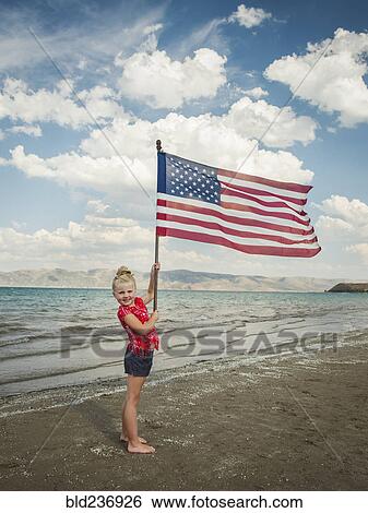 Stock Photograph - Caucasian girl holding American flag at beach. Fotosearch