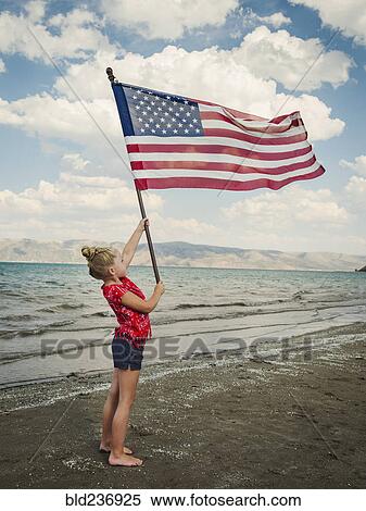 Stock Photography - Caucasian girl holding American flag at beach. Fotosearch