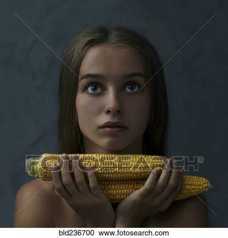 Stock Image - Caucasian girl holding corn on cob and looking up. Fotosearch
