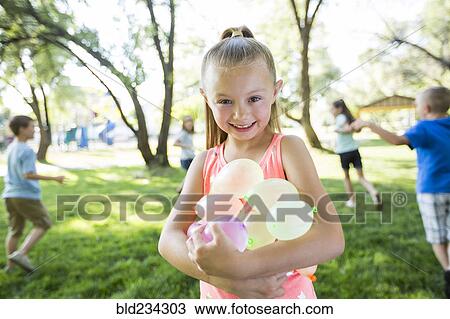 Stock Image - Caucasian girl holding water balloons. Fotosearch