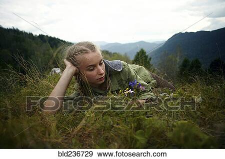 Stock Photo - Caucasian girl holding wildflowers laying in grass on hill. Fotosearch