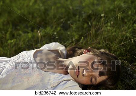 Stock Image - Caucasian girl laying in grass with eyes closed. Fotosearch