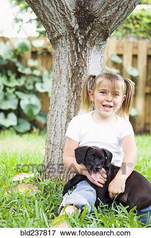 Stock Photo - Caucasian girl leaning on tree hugging dog. Fotosearch