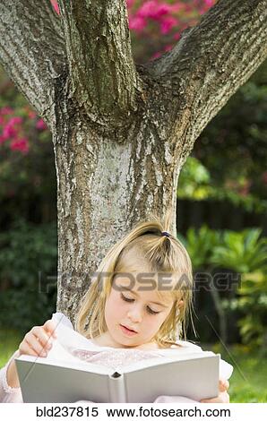 Caucasian girl leaning on tree reading book View Large Photo Image Stock Photography - Caucasian girl leaning on tree reading book. Fotosearch