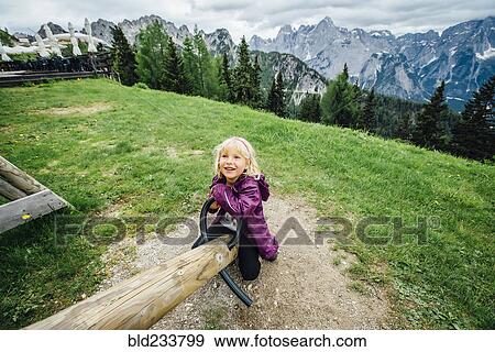 Stock Photo - "Caucasian girl on seesaw near mountain range, Tarvisio, Vienna, Austria". Fotosearch
