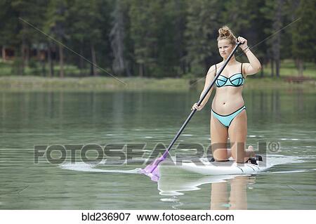 Stock Photo - Caucasian girl paddleboarding on lake. Fotosearch