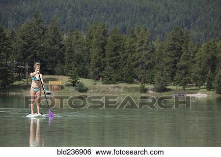 Stock Photograph - Caucasian girl paddleboarding on lake. Fotosearch