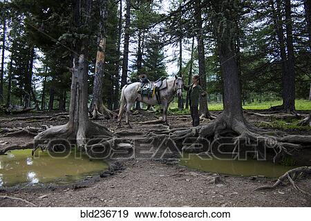Stock Photo - Caucasian girl petting horse in forest near puddles. Fotosearch