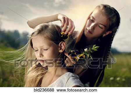 Stock Photo - Caucasian girl placing flower in hair of sister. Fotosearch
