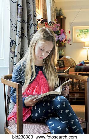 Stock Image - Caucasian girl reading book in armchair. Fotosearch