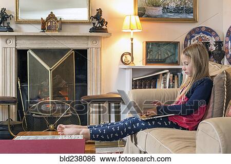 Stock Photograph - Caucasian girl sitting on sofa using laptop. Fotosearch