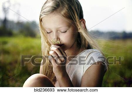 Stock Image - Caucasian girl smelling wildflower in field. Fotosearch