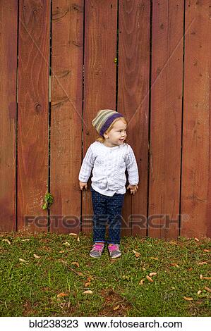 Stock Image - Caucasian girl standing near wooden fence. Fotosearch