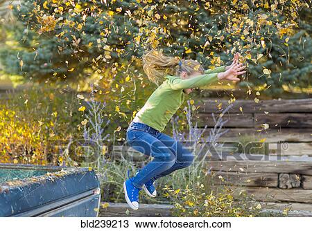 Stock Image - Caucasian girl throwing autumn leaves and jumping off truck. Fotosearch