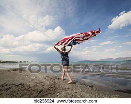 Picture - Caucasian girl walking with American flag at beach. Fotosearch