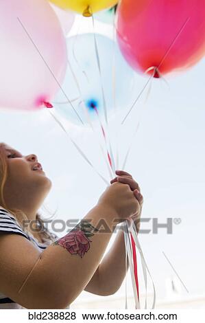 Stock Photo - Caucasian girl with temporary arm tattoo holding balloons. Fotosearch