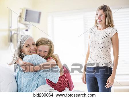 Picture - Caucasian granddaughter hugging grandmother in hospital. Fotosearch